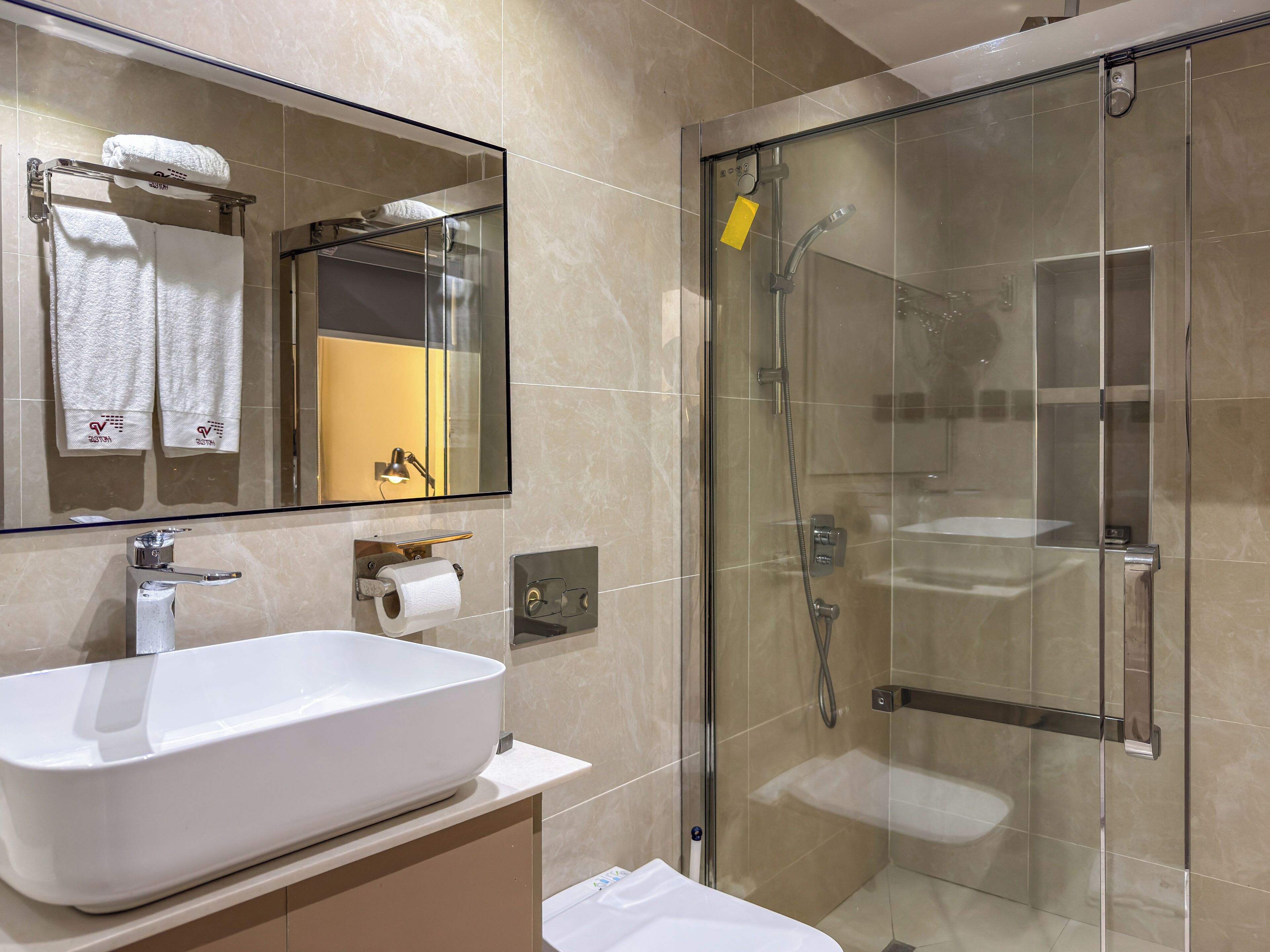 A modern bathroom with a large mirror, a white sink, a glass-enclosed shower, and a towel rack with towels.