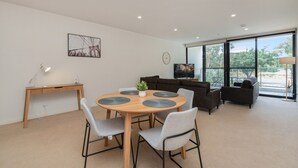 A modern living room with a round wooden table, grey chairs, a dark sofa, and a television.