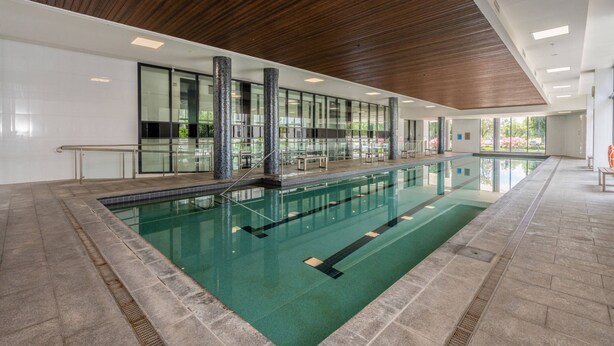 A modern indoor swimming pool with clear lanes, wooden ceiling, and large windows.
