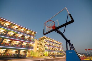 Um edifício de vários andares com varandas, uma cesta de basquete e uma placa com a inscrição 'APEX'.