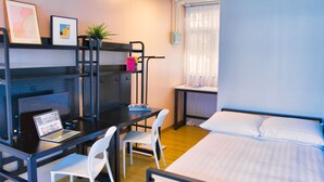 A compact room with a bed, a desk with a laptop, two chairs, a small shelf with books, and a window with curtains. - Runway 1331 - Enlight Youth Hostel (Kowloon)