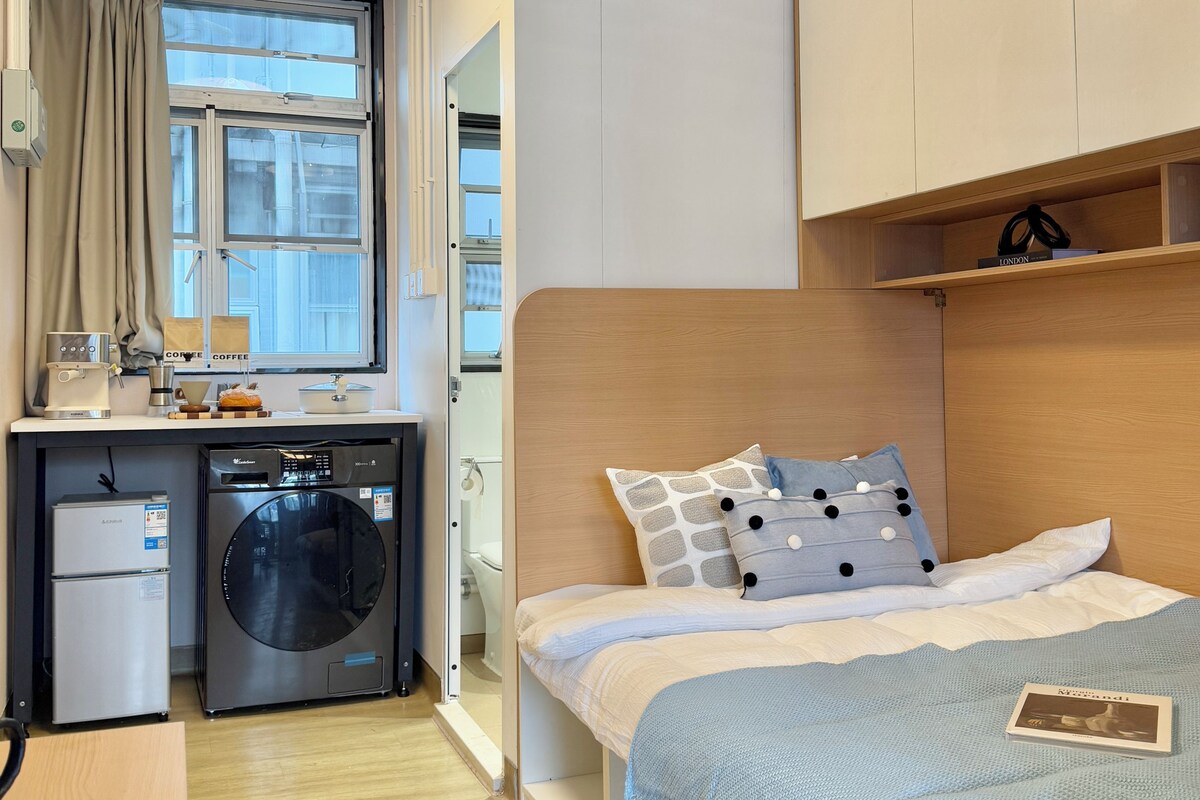 Une chambre compacte comprenant un lit, un lave-linge et une petite kitchenette.