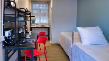 A room with a desk, two beds, a red chair, and a window with curtains.