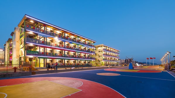 A multi-story building with balconies, a basketball court, and a street sign indicating 14th Street. - Runway 1331 - Enlight Youth Hostel (Kowloon)