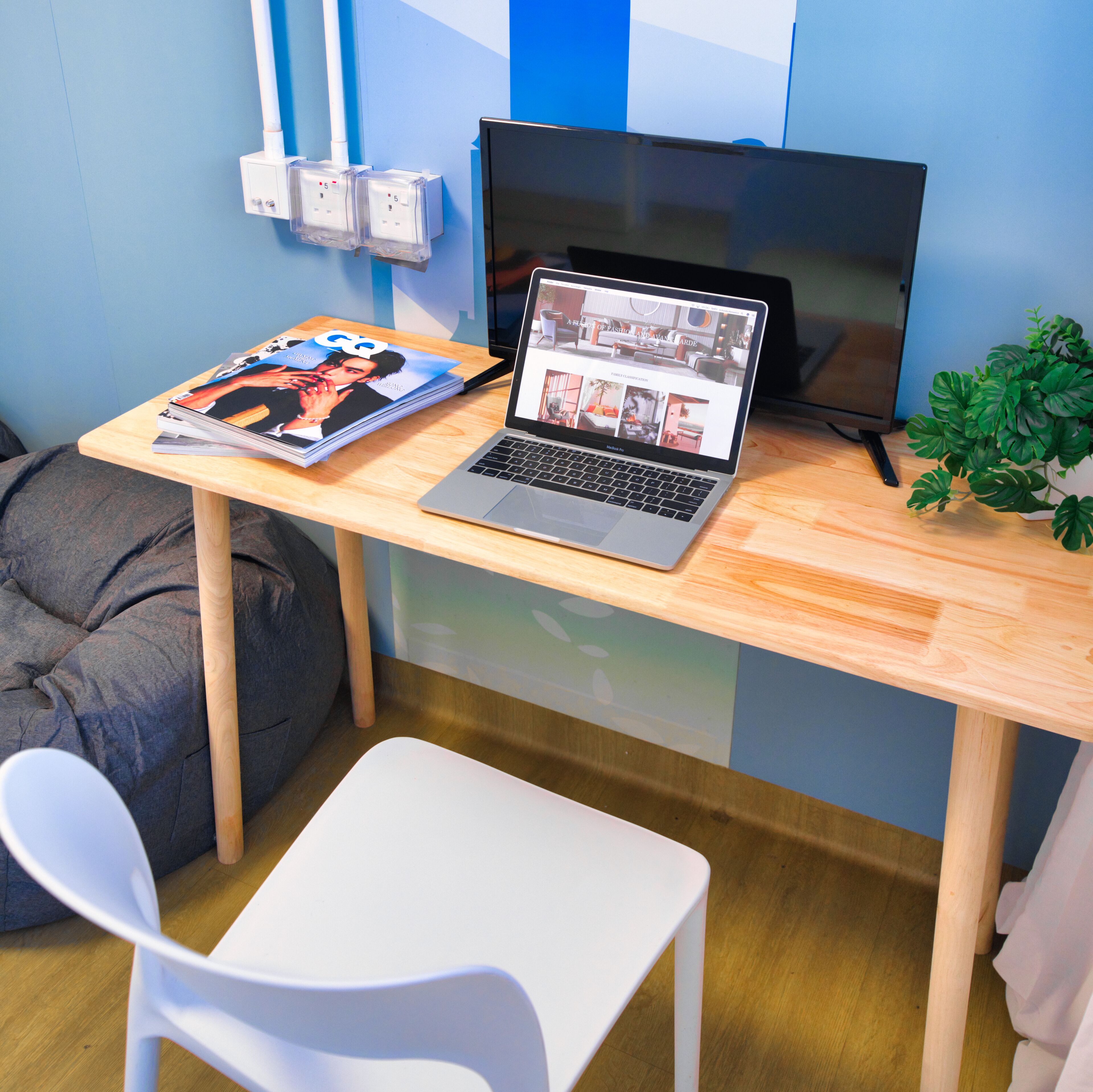 A workspace with a laptop, a magazine, a plant, and a bean bag chair.