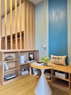 A modern interior with wooden shelving, a round table with a vase, and a pillow with 'iRent Hong Kong' text. - Runway 1331 - Enlight Youth Hostel (Kowloon)