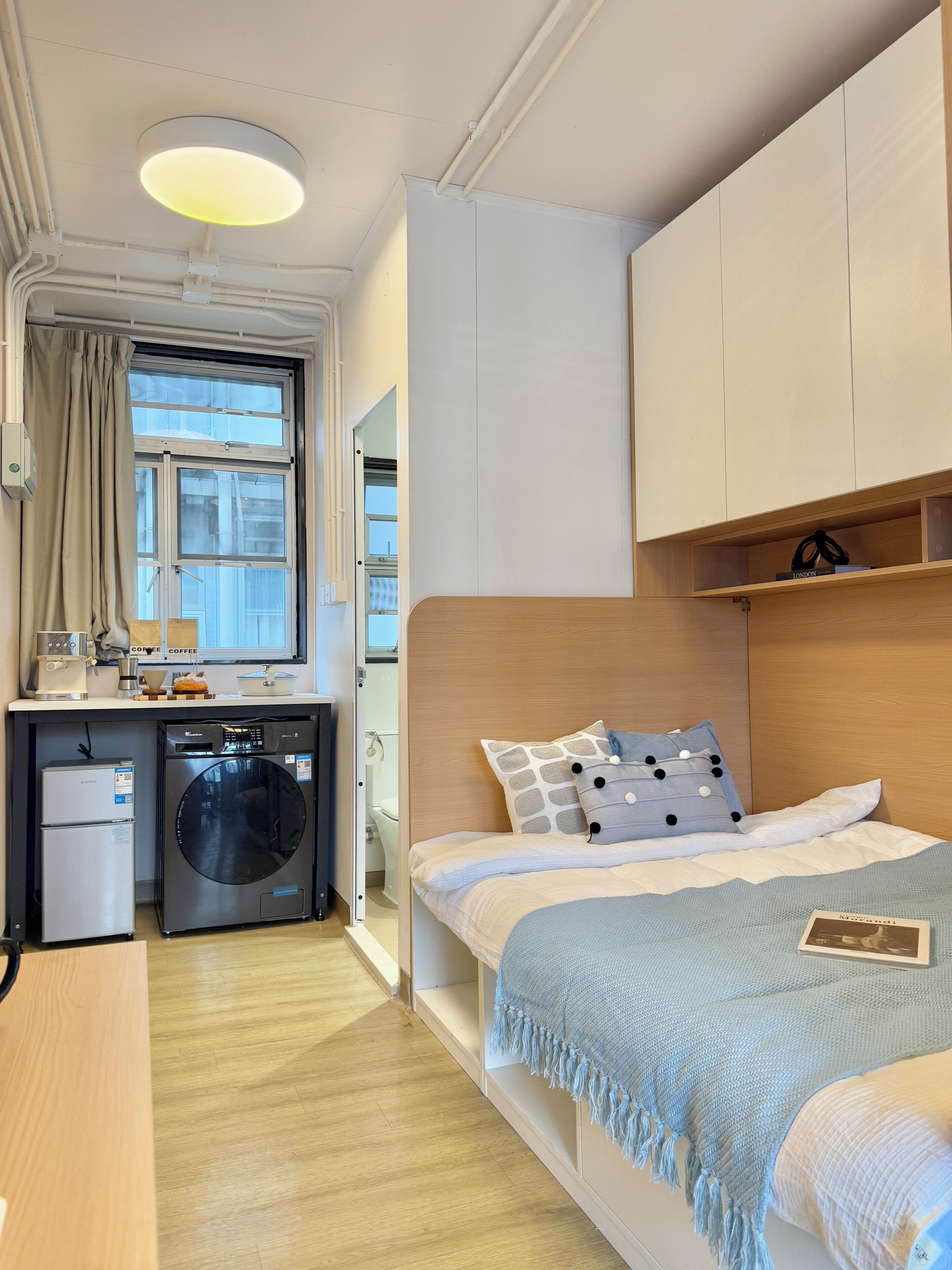 A compact bedroom with a bed, a washing machine, and a small kitchenette.