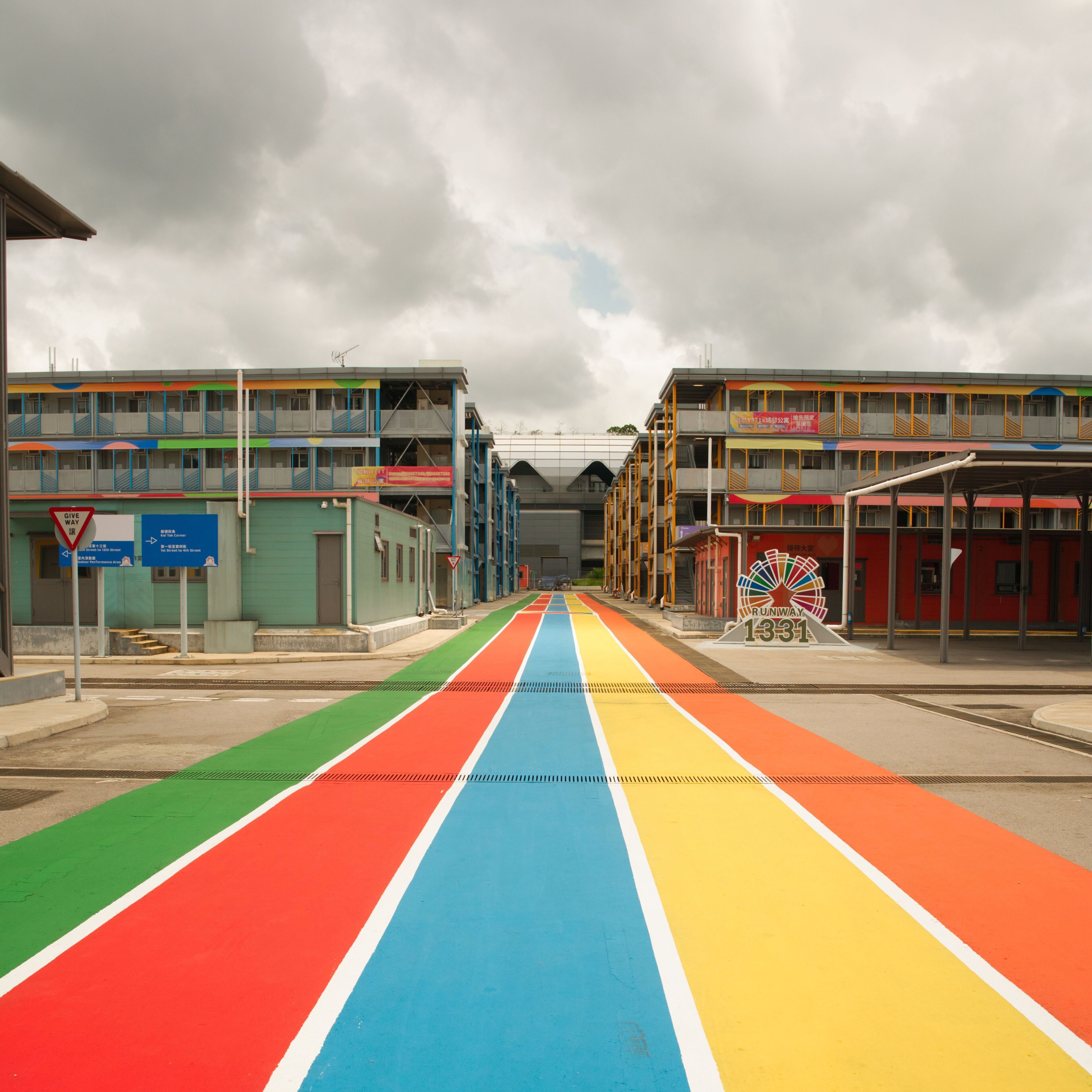 Un immeuble à plusieurs étages, avec une passerelle piétonne aux couleurs vives qui mène à une gare.