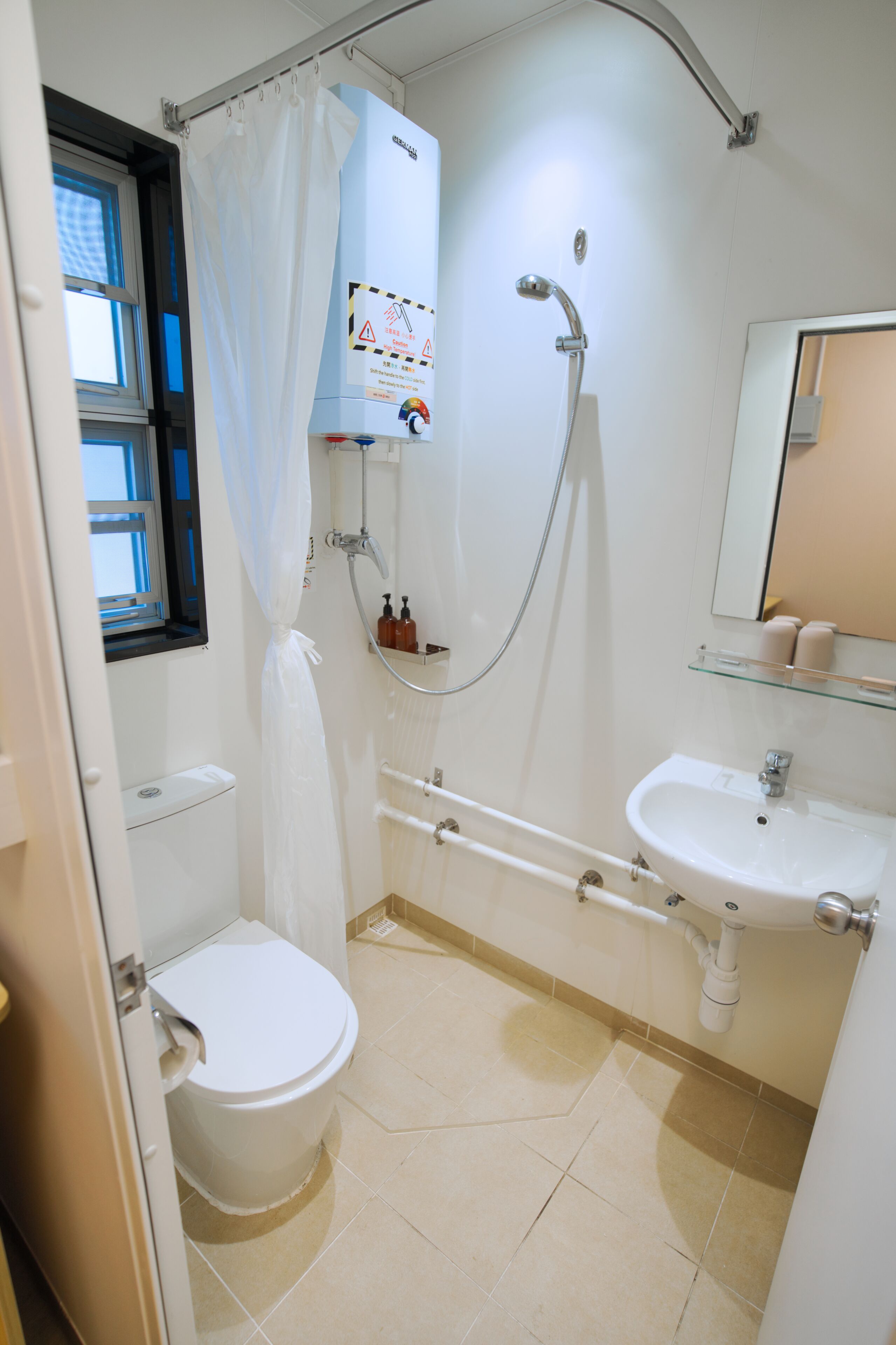 Een badkamer met toilet, douche, wastafel en raam.