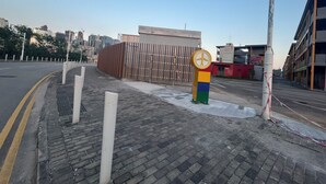 A paved walkway with a colorful pole, a fence, and buildings in the background. - Runway 1331 - Enlight Youth Hostel (Kowloon)