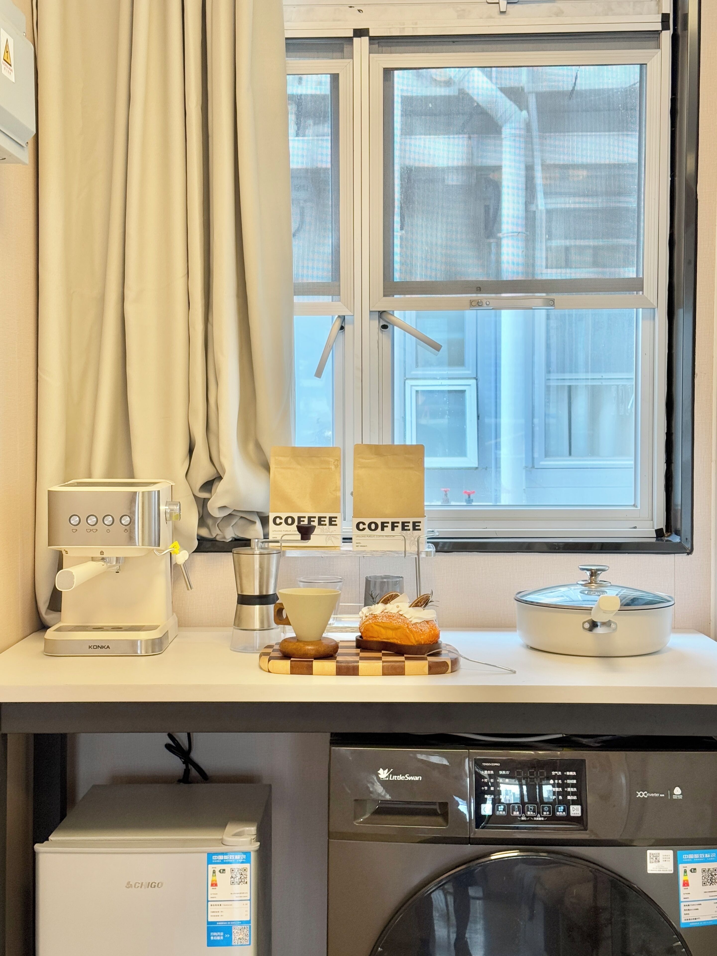 Una kitchenette con cafetera, una taza, un pastel y un microondas.