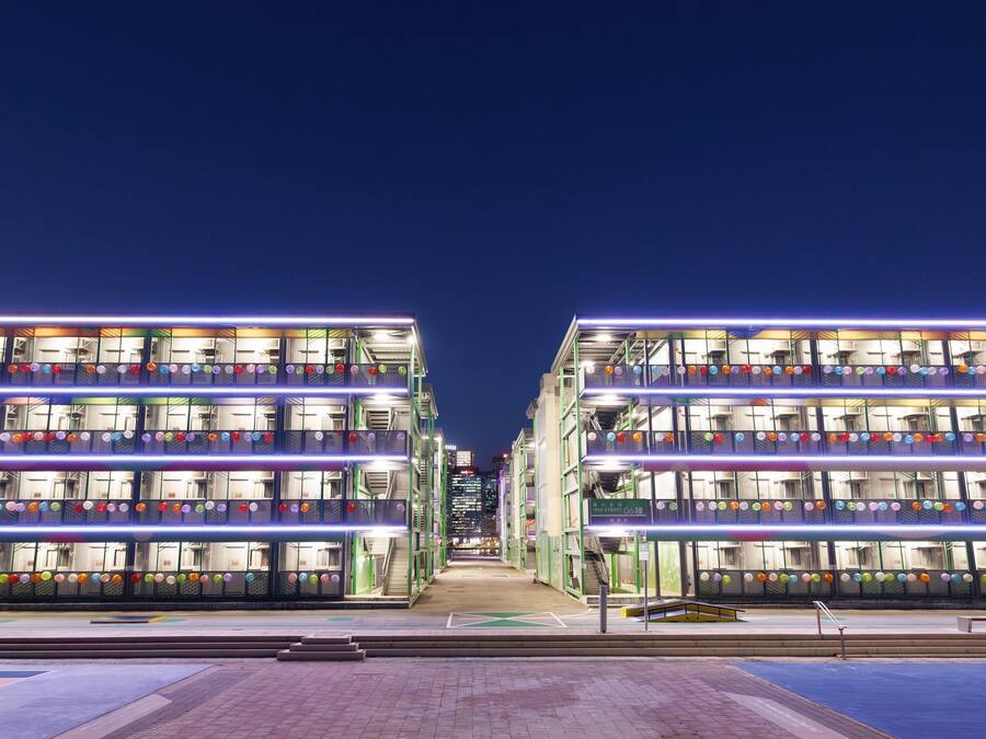 A multi-story building with balconies, a central walkway, and a sports court area.