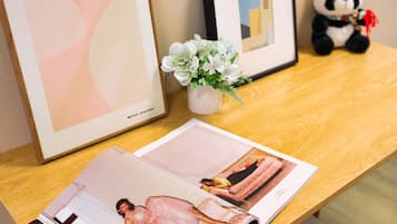 A wooden table with a magazine, a framed abstract painting, a framed geometric painting, a small vase with white flowers, and a panda plush toy.