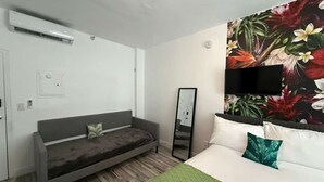 A hotel room with a bed, a sofa, a flat-screen TV, a mirror, and a floral wall mural. - Indian Creek (Miami Beach)