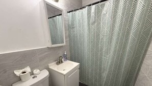 A bathroom with a toilet, sink, and shower curtain. - Indian Creek (Miami Beach)