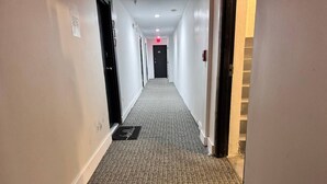 A hotel hallway with carpeted floors, white walls, and doors leading to rooms. - Indian Creek (Miami Beach)