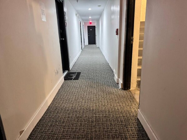 Un couloir d'hôtel avec des revêtements de sol en moquette, des murs blancs et des portes donnant accès aux chambres.