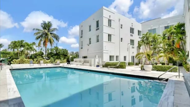 A modern building with a pool, surrounded by palm trees and greenery. - Indian Creek (Miami Beach)