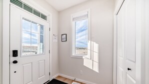 Ein heller, moderner Eingangsbereich mit einer weißen Tür, einem kleinen Fenster und einer schwarzen Fußmatte.