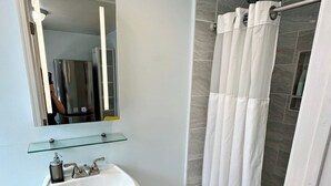 A bathroom with a pedestal sink, a glass shelf above it, a shower with a white curtain, and a tiled floor. - Welcoming studio in El Cerrito for a cozy getaway (El Cerrito)