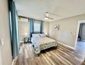 A bedroom with a bed, a ceiling fan, a nightstand, a lamp, and a window with curtains.