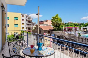 A balcony with a table, chairs, and a view of a pool area.