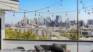 A rooftop terrace with a city skyline view, string lights, and outdoor furniture.