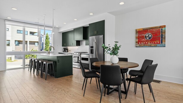 A modern kitchen with dark green cabinets, stainless steel appliances, and a central island with bar stools.