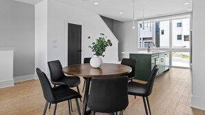 A modern dining area with a round wooden table, black chairs, and a white vase with a plant.
