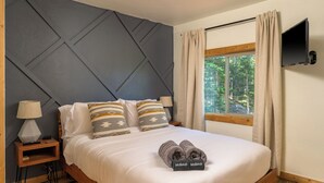 Ein ordentlich bezogenes Bett mit Kopfteil, ein Nachttisch mit Lampe und ein an der Wand befestigter Fernseher.