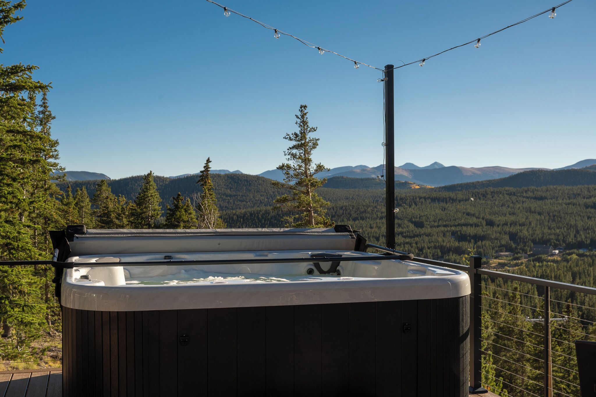Un bain à remous sur une terrasse offrant une vue sur une chaîne de montagnes boisées.