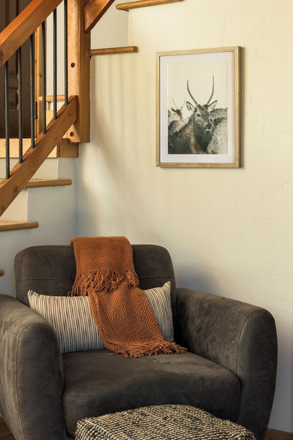 A room with a gray sofa, a wooden staircase, and a framed wildlife illustration on the wall. - Skyline Lodge (Idaho Springs)