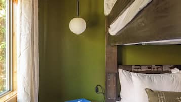 Una cama litera con cabecera de madera, una mesita con un libro y una lámpara colgante en una habitación con paredes verdes y suelo de madera.