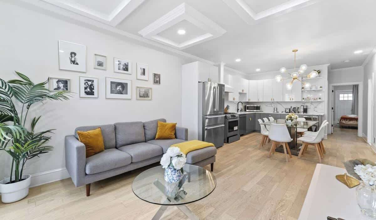A modern living room with a grey sofa, a glass coffee table, and a dining area with white chairs.