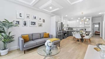 A modern living room with a grey sofa, a glass coffee table, and a dining area with white chairs.