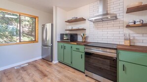 A modern kitchen with green cabinets, a stainless steel refrigerator, a microwave, and a built-in oven. There is a window providing natural light and a view of trees outside. - Cedar Flat Cabin - Outdoor Fire Pit! (Carnelian Bay)