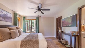 A bedroom with a bed, a ceiling fan, a view of trees through a window, and a wooden floor. - Cedar Flat Cabin - Outdoor Fire Pit! (Carnelian Bay)