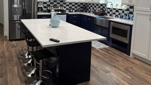 A modern kitchen with white cabinets, a black island, stainless steel appliances, and a checkered backsplash. - AG Ranch in Hempstead (Hempstead)