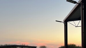 A concrete patio area with a view of a sunset over a grassy field and a building with a red roof. - AG Ranch in Hempstead (Hempstead)