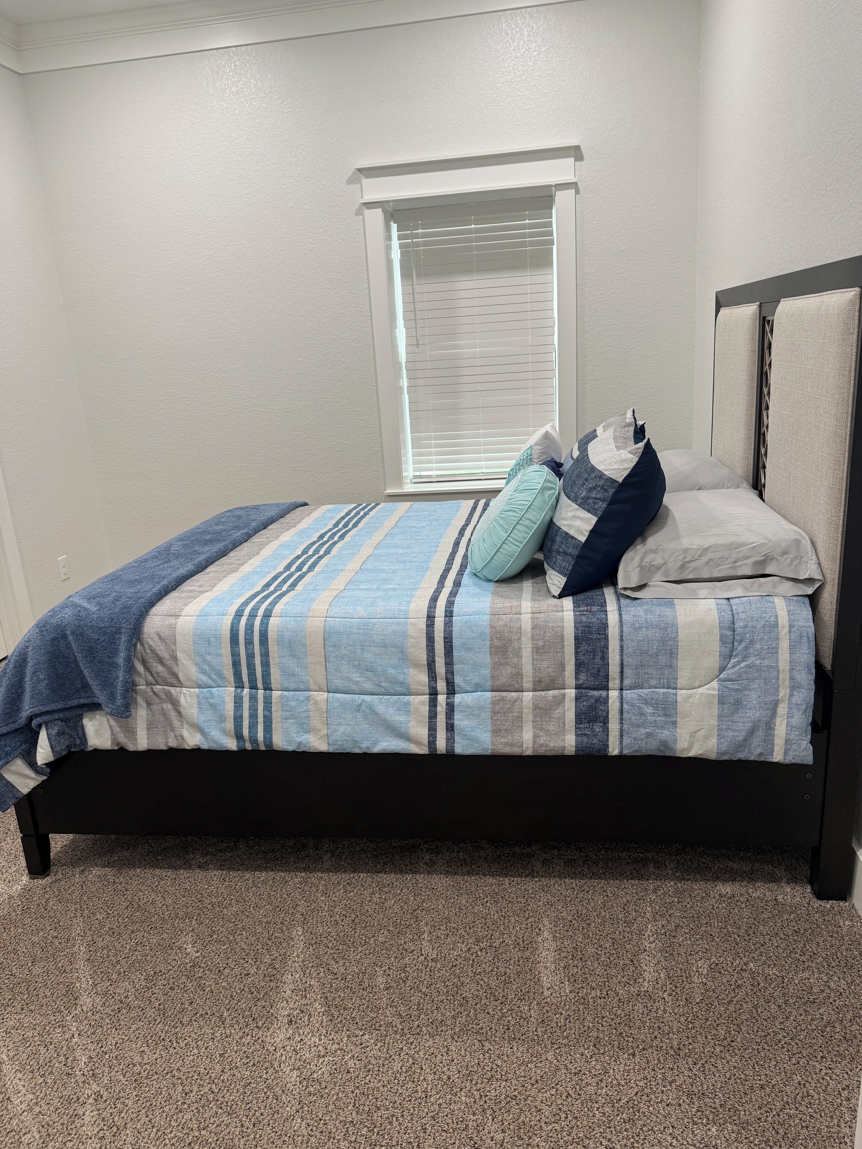 Een slaapkamer met een bed, een raam en een tapijtvloer.
