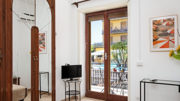 Habitación de hotel con balcón, televisión, una mesita y un cuadro en la pared.