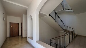 Un interior espacioso con piso de mármol, una escalera con barandales negros y una puerta de madera.