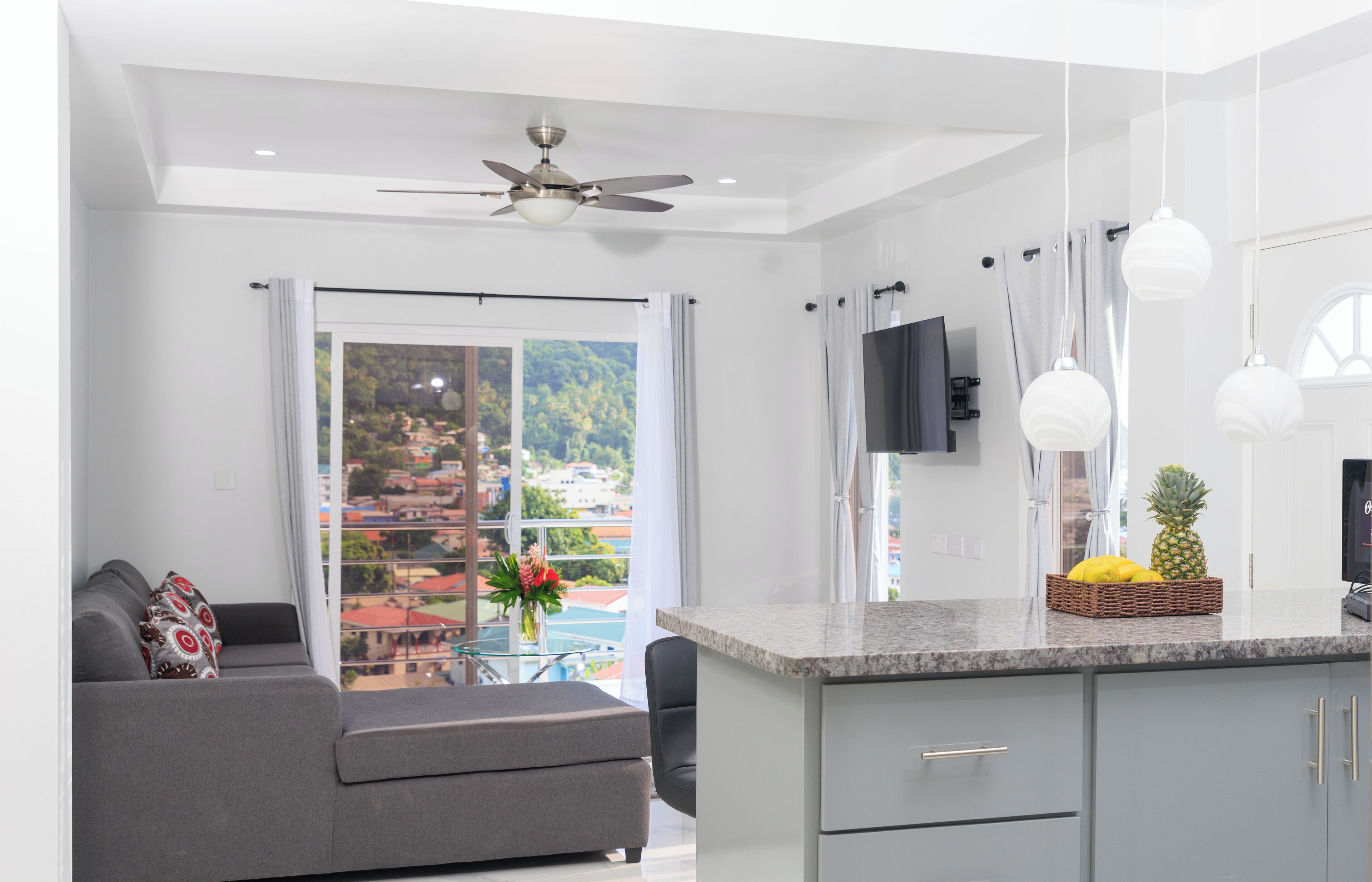 A modern kitchen with a granite countertop, grey cabinets, and a dining area with a grey sofa and a small table.