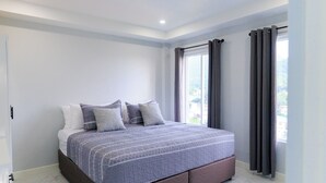 Une chambre moderne avec un grand lit, une vue sur l’extérieur par une fenêtre et une porte située à gauche.