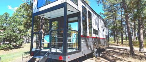 A modern camper with a two-level deck, a ladder for access, and a spacious interior.