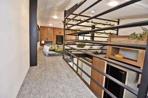 A narrow hallway with a bunk bed, a wooden cabinet, and a small table with a plant. - The Ponderosa Perch, a modern tiny home nestled in the pines of Elizabeth (Elizabeth)