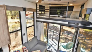 Interior moderno de um veículo recreativo, com cama no mezanino, sofá e área de jantar.
