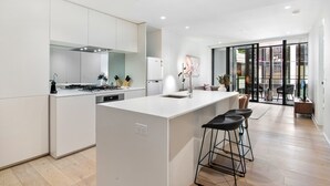 A modern kitchen with a central island, bar stools, and a view to the dining area. - Spacious Modern Apartment With Pool & Gym Access (Melbourne)