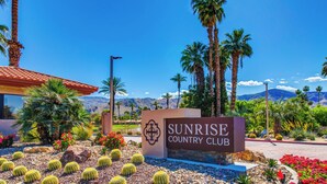 Skilt for Sunrise Country Club med et ørkenlandskab og kaktusser i forgrunden.