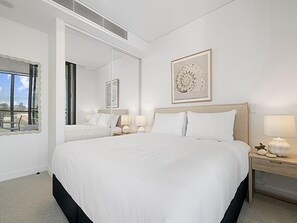 A hotel room with a large bed, a nightstand with a lamp, a mirror, and a framed picture on the wall. - Bright 1-bedroom Escape With Private BBQ (Perth)